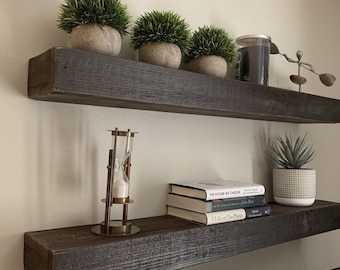 May include: Two dark brown wooden shelves with a variety of decorative items, including potted plants, books, and a small hourglass. The shelves are mounted on a white wall.