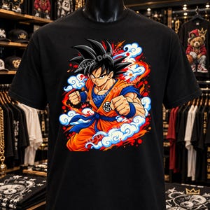 May include: A black short-sleeve t-shirt featuring a graphic print of a spiky-haired character in an orange and blue martial arts uniform. The character is surrounded by stylized blue clouds and red energy bursts, with a Japanese kanji symbol on the chest.