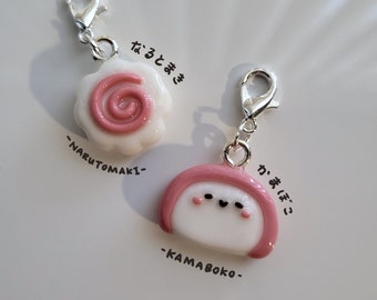 Peut inclure: Deux pendentifs de charme rose et blanc avec des anneaux de saut argentés. Le premier charme est un tourbillon rose sur fond blanc avec le texte "narutomaki" et "なるとまき" en noir. Le deuxième charme est un kamaboko rose et blanc avec un visage et le texte "kamaboko" et "かまぼこ" en noir.