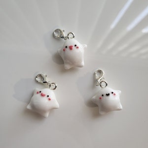 Può includere: Tre ciondoli bianchi a forma di stella con facce sorridenti e guance rosa. Ogni ciondolo ha un anello argentato per attaccarlo a una borsa, un portachiavi o un altro oggetto.