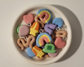 Könnte beinhalten: Eine Sammlung bunter Ton-Anhänger in verschiedenen Formen, darunter Herzen, Regenbögen, Kleeblätter und ein Hut. Die Anhänger sind alle handgefertigt und haben eine glänzende Oberfläche.