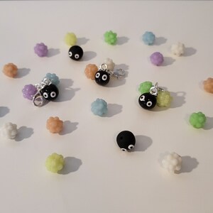 Könnte beinhalten: Eine Sammlung von schwarzen und weißen Charm-Perlen mit Glitzern und bunten Perlen in verschiedenen Grüntönen, Lila und Orange. Die Charms sind an silbernen Sprungringen befestigt.