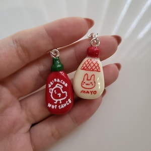 May include: Two small ceramic bottle charms, one red with a white chicken and the words "Sriracha Hot Sauce" and the other white with a red bunny and the word "Mayo".