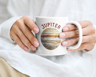 May include: White ceramic mug featuring a detailed illustration of Jupiter, with its swirling bands of orange, brown, and white. The word "JUPITER" is printed in a brown, rounded font above the planet image. A classic coffee mug design.