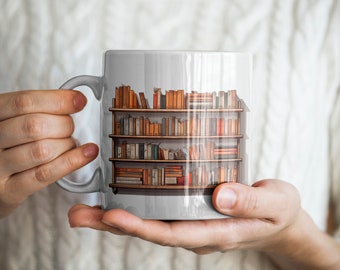 Puede incluir: Una taza de cerámica blanca con un diseño impreso de una estantería llena de libros coloridos.