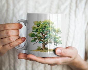 Könnte beinhalten: Eine weiße Keramiktasse mit einem Aquarellgemälde eines großen Baumes. Der Baum hat grüne Blätter und einen braunen Stamm. Die Tasse hat einen gebogenen Henkel und wird von einer Person gehalten, die einen weißen Pullover trägt.