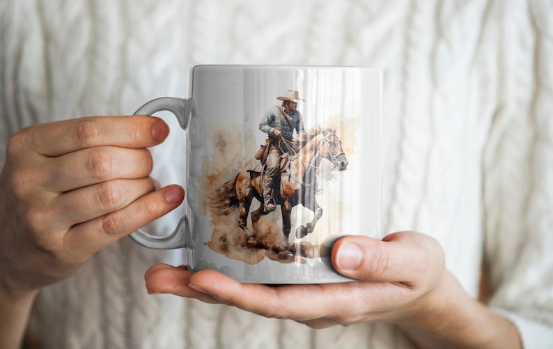 May include: A white ceramic mug with a watercolor illustration of a cowboy riding a brown horse. The cowboy is wearing a brown hat and a blue shirt. The horse is running and its mane is flowing in the wind.