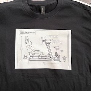 May include: Black t-shirt with a white schematic diagram of a single-sim racing rig. The diagram includes measurements in inches and features a racing seat, steering wheel, and pedal face.