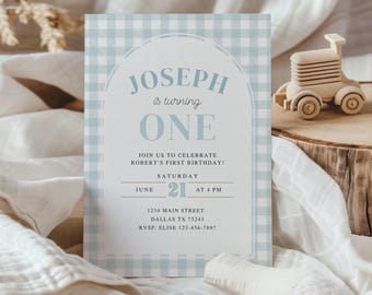May include: A light blue and white gingham patterned birthday invitation with the text "JOSEPH is turning ONE". The invitation includes the date, time, and location of the party. A wooden toy tractor sits on a wooden surface.