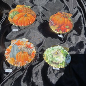 May include: Four decorative scallop shells featuring decoupage autumn designs. Each shell displays vibrant orange pumpkins, colourful fall leaves, and harvest motifs with gold-painted edges. Small white labels marked SS, O, MM, and NN are placed near each shell.