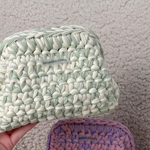 May include: Two crocheted bags, one green and white, the other pink and purple. Both bags have a label that says "tatianka.crafts".