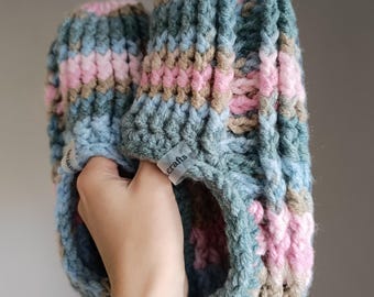 May include: A pair of knitted slippers in shades of blue, pink, and brown. The slippers have a striped pattern and are held in a hand. The tag on the slipper reads "crafts".