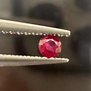 Peut inclure: Gros plan d'une pierre précieuse rouge vif tenue dans des pinces. La pierre précieuse est ronde et facetée.