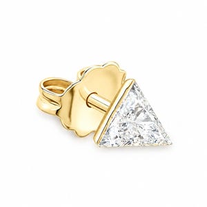 May include: A gold stud earring featuring a triangular-cut clear gemstone set in a polished gold metal frame. The earring includes a matching gold butterfly-style friction back post, showcasing a clean, geometric design with a faceted stone.