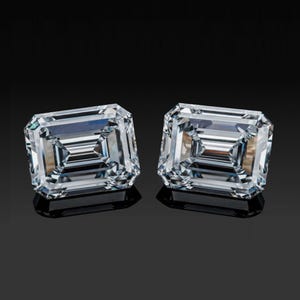 May include: Two emerald-cut diamonds, each with a clear, brilliant appearance. The gems are set against a black background, highlighting their facets and internal reflections. The diamonds are rectangular with cut corners, reflecting light.