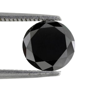 Pode incluir: Uma gema de diamante preta redonda mantida em pinças. O diamante tem um corte facetado e é muito brilhante.