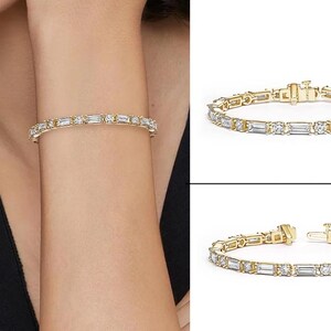 Op de afbeelding: Een gouden armband met rechthoekige en ronde heldere edelstenen. De armband wordt om een pols en apart getoond. De armband heeft een veilige sluiting en een klassiek ontwerp.