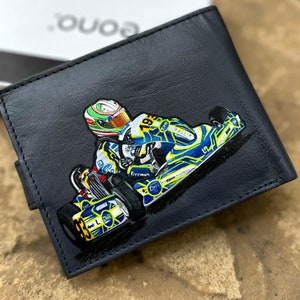 May include: A black leather wallet featuring a painted image of a go-kart racer wearing a helmet and racing suit. The go-kart is yellow, blue and black with the number 193 on the side. The words "Freeman" and "DHR" are also visible on the go-kart.