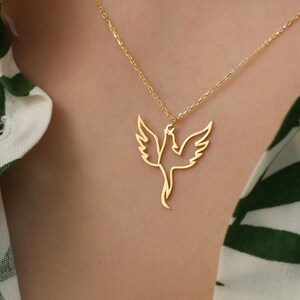 May include: A gold necklace with a delicate, openwork pendant shaped like a bird in flight. The pendant is a simple outline of a bird with its wings spread wide.