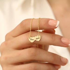 May include: Gold necklace with two heart pendants. The hearts are engraved with the names "Dina" and "Perla".