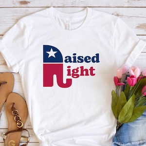 May include: White t-shirt with a red, white, and blue elephant graphic and the text "raised right".
