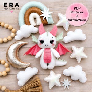 May include: A felt craft kit featuring a white dragon with pink wings and horns, surrounded by felt clouds, a rainbow, a gold crescent moon, and stars. A pink circular label displays the text PDF Patterns + Instructions in black font.