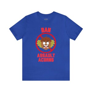 May include: A royal blue t-shirt with a red circle and a line through it. Inside the circle is a cartoon acorn with a face and the words "Ban Assault Acorns".