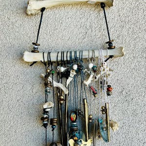 Pode incluir: Uma decoração de parede única com elementos naturais de osso e madeira. O design incorpora várias contas, amuletos e peças decorativas suspensas de estruturas ósseas. A paleta de cores inclui tons naturais, preto e detalhes metálicos, criando uma estética rústica.