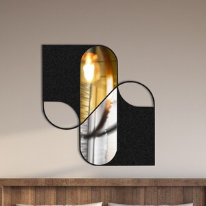 May include: A modern bedroom with a wooden bed frame and white bedding. A black and gold geometric mirror hangs on the wall above the bed. The room has a large window with a view of snow-covered mountains.