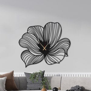 Puede incluir: Reloj de pared de metal negro en forma de flor estilizada con agujas doradas. El reloj está montado en una pared blanca en un salón.