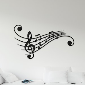 May include: Black metal wall decor featuring a treble clef and musical notes. The decor is mounted on a white wall above a white sofa and two brown coffee tables.