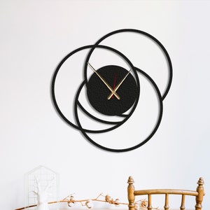 Pode incluir: Um relógio de parede moderno com um design circular em preto e branco. O relógio tem três círculos sobrepostos, sendo o círculo central preto e os dois círculos exteriores brancos. Os ponteiros do relógio são dourados.