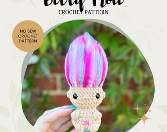 May include: A crocheted troll doll with pink, blue, and white yarn hair. The doll is holding a pink star in its hand. The doll is sitting on a hand. The image has the text "Bitty Troll Crochet Pattern" and "No Sew Crochet Pattern".