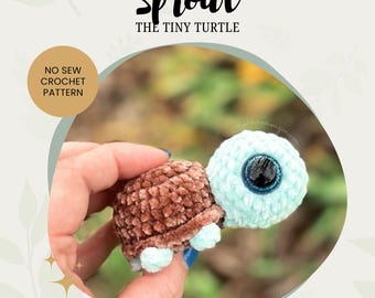May include: A crocheted turtle amigurumi toy named "Sprout the Tiny Turtle". The turtle is light blue with brown crocheted shell and large blue eyes. The toy is being held in a hand.