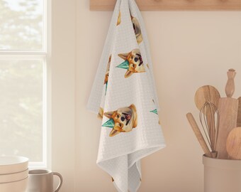 Puede incluir: Paño de cocina blanco con un patrón repetido de un corgi con un gorro de fiesta. El corgi es marrón claro y blanco con una expresión feliz. El paño está colgado en un estante de madera en una cocina.