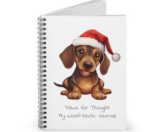 Könnte beinhalten: Ein spiralgebundenes Notizbuch mit einem weißen Einband, auf dem ein Cartoon-Dackel mit einem roten Weihnachtshut zu sehen ist. Der Text "Paws for Thought: My woof-tastic Journal" ist unter dem Bild gedruckt.