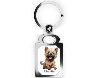 Puede incluir: Llavero de plata con una etiqueta rectangular que presenta un perro de dibujos animados con pelaje marrón y blanco. El perro lleva un collar marrón y tiene una expresión feliz. El texto "Charlie" está impreso debajo del perro.