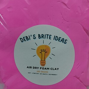 May include: A pink air dry foam clay in a clear plastic bag with a white label that says "DEBI'S BRITE IDEAS" with a lightbulb graphic and "AIR DRY FOAM CLAY 100 GRAMS SOFT - STRETCHY - DIY CRAFTS - KID FRIENDLY".