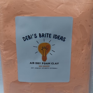 May include: A sealed bag of orange air dry foam clay. The bag has a label that reads "DEBI'S BRITE IDEAS" with a lightbulb graphic and the text "AIR DRY FOAM CLAY 500 GRAMS SOFT - STRETCHY - DIY CRAFTS - KID FRIENDLY".