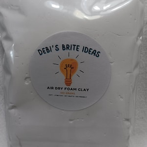 May include: A white bag of air dry foam clay with a yellow lightbulb logo and the text "DEBI'S BRITE IDEAS" and "AIR DRY FOAM CLAY 100 GRAMS SOFT STRETCHY DIY CRAFTS KID FRIENDLY".