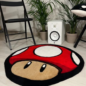May include: A red and white mushroom-shaped rug with black outlining. The rug has a brown face with two black eyes.