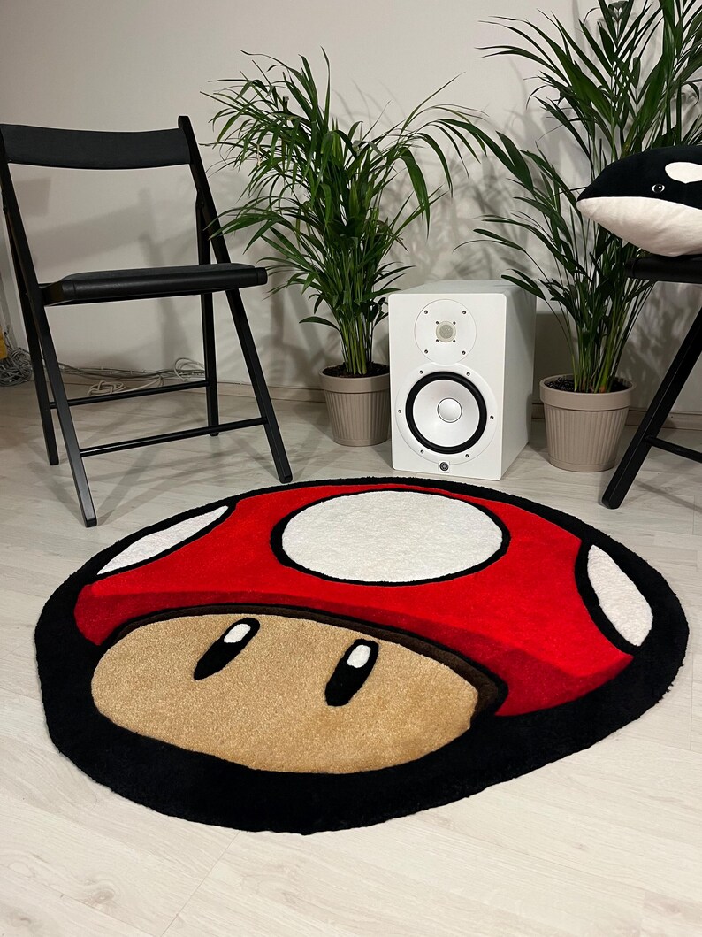 May include: A red and white mushroom-shaped rug with black outlining. The rug has a brown face with two black eyes.