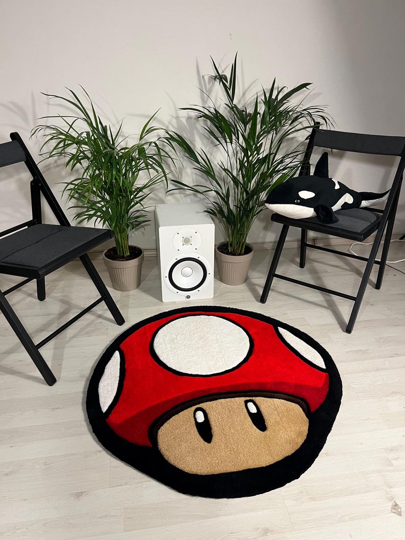 May include: A red and white mushroom-shaped rug with a black outline. The rug is on a light wood floor. There are two black folding chairs and two potted plants in the background.