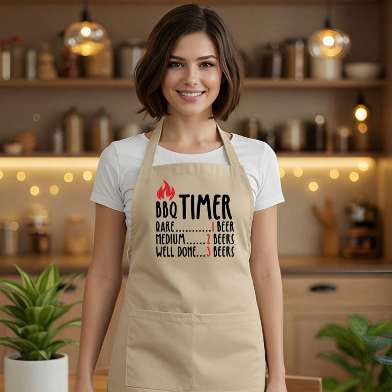 May include: A tan apron with a pocket and the text "BBQ TIMER" in black with a red flame graphic. The text below lists "Rare...1 Beer", "Medium...2 Beers", and "Well Done...3 Beers".