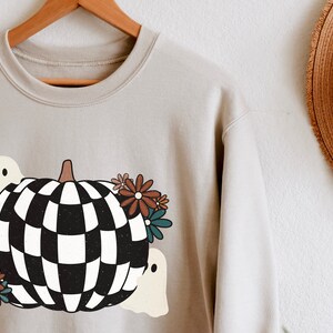May include: A light gray sweatshirt with a checkered pumpkin design, two ghosts, and floral accents.