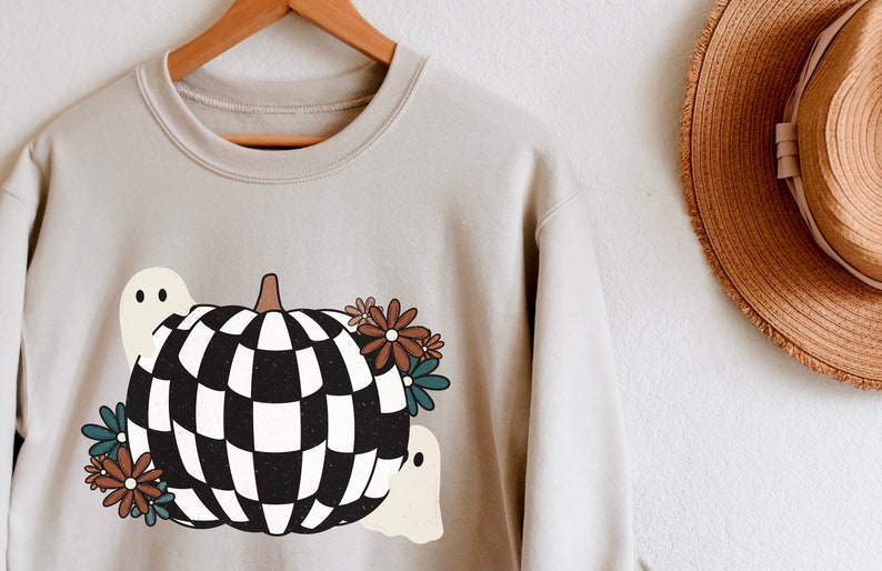 May include: A light gray sweatshirt with a checkered pumpkin design, two ghosts, and floral accents.