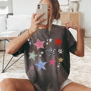 Comfort Colors 1717 T-Shirt
Color: Pepper (textured gray)
Graphic: Colorful collage-style star graphic featuring various hand-drawn and patterned stars scattered across the chest. The stars include a mix of animal prints, stripes, solid colors, and textures, with some metallic and doodle-like accents.
keywords: early 2000s, y2k streetwear, cool girl aesthetic, baddie, whimsigoth, whimsical, whimsy goth tops, soft grunge, summer outfit, music festival, rave, alt clothing, trending tops women