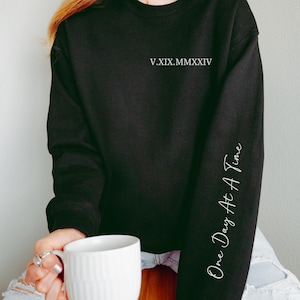 May include: Black sweatshirt with the text "V.XIX.MMXXIV" on the front and "One Day At A Time" on the sleeve.