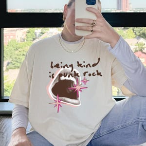 Comfort Colors 1717 Shirt
Color: Ivory (cream, off white)
Graphic: open screaming mouth in a retro halftone print, surrounded by pink stars and starbursts, with the handwritten phrase “Being Kind is Punk Rock” above in brown lettering
Title: Being Kind Is Punk Rock Shirt, Retro Streetwear Tee, Oversized Y2K, Soft Grunge, Kindness Quote, Alt Clothing, Comfort Colors Unisex