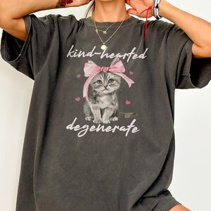 Comfort Colors 1717 Shirt
Color: Pepper (textured gray)
Graphic: Illustration of a gray tabby kitten sitting with a large pink bow tied on its head. The kitten is surrounded by small pink hearts and framed by the handwritten-style phrase "kind-hearted degenerate" in soft, playful lettering.
keywords: soft girl aesthetic, baddie, cool girl, early 2000s aesthetic, downtown girl outfit, unhinged humor, vintage, soft grunge, edgy graphic tee, alternative fashion, bow coquette, millennium, pastel